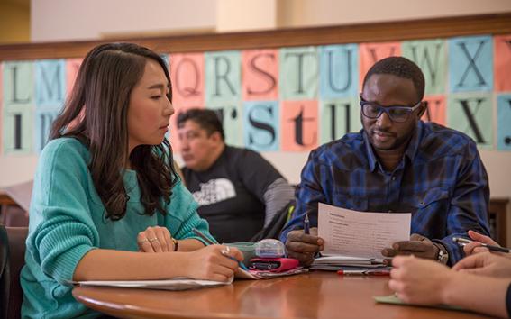 Two people speaking to each other in classroom with alphabet behind them.