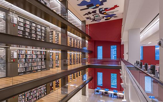 Interior view of library showing 5 floors filled with book shelves, a large mural on ceiling, and a red wall lined with windows.